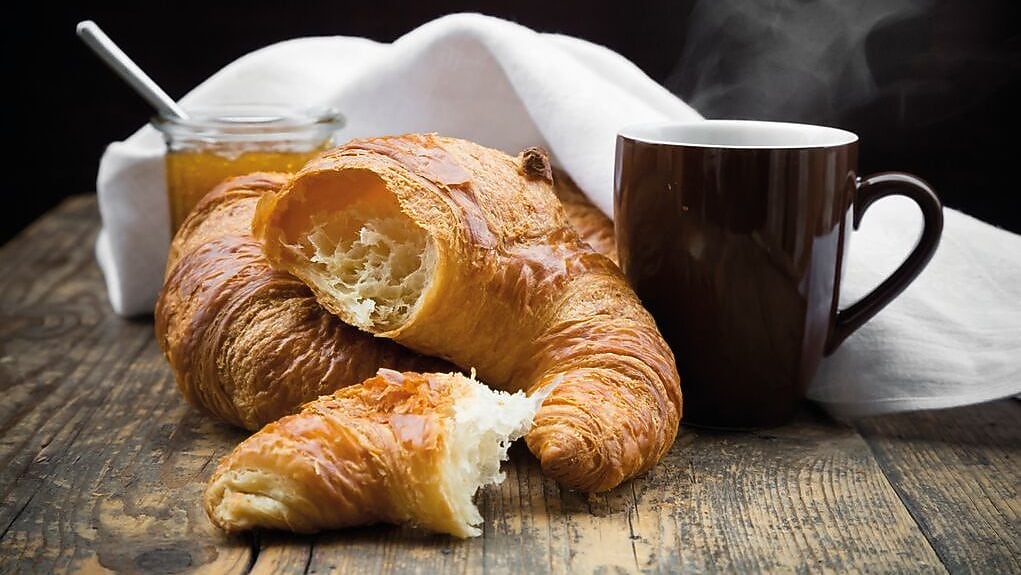 Croissant with coffee and honey on a wooden table.