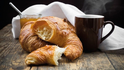 Croissant with coffee and honey on a wooden table.