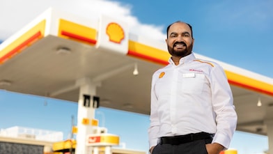 Man in a white uniform stands smiling in front of a Shell Mobility station