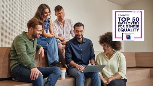A group of five people are sitting on wooden steps in a modern, indoor setting.