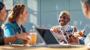Four diverse colleagues engage in a lively discussion around a table with laptops