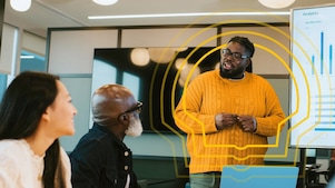 A person in a yellow sweater presents analytics on a screen to two colleagues in an office.