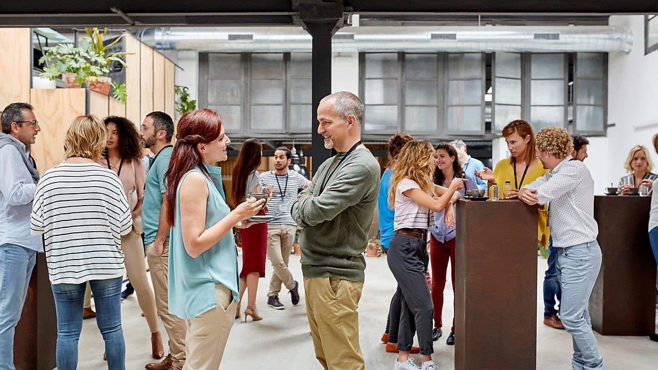 A lively office social event with diverse people conversing and drinking coffee.