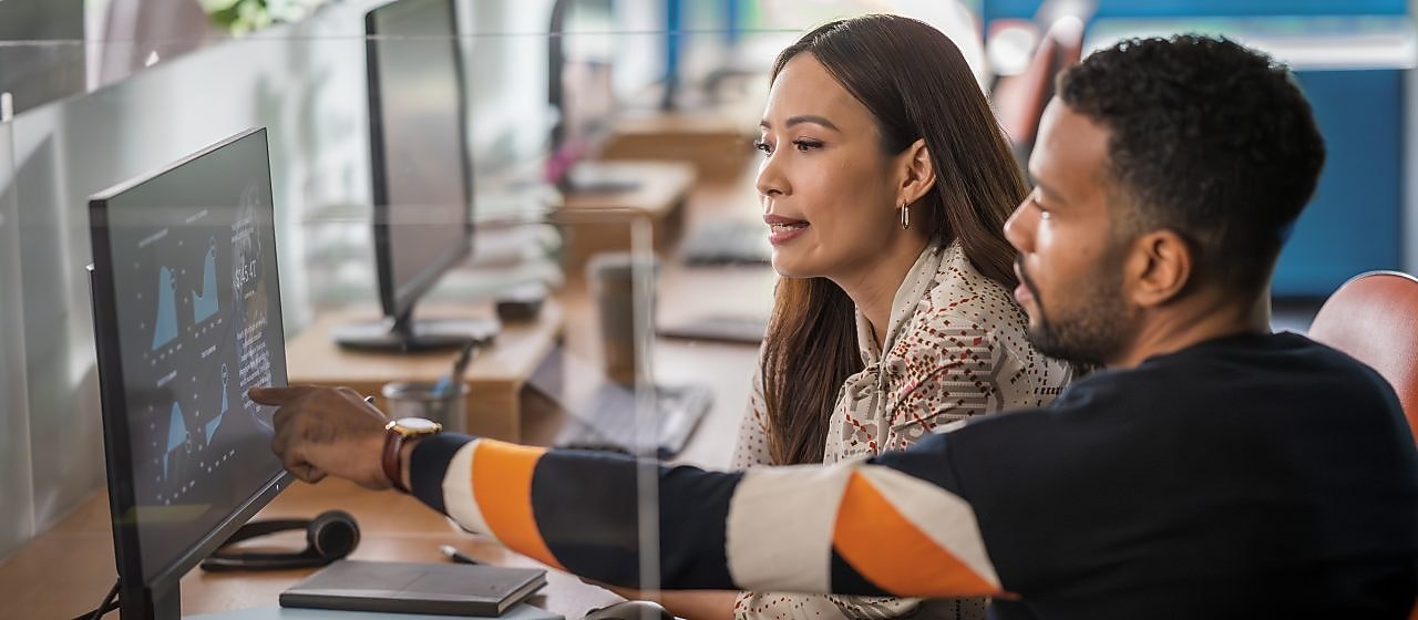 Two colleagues sitting at a desk collaborate while reviewing data visualizations on a computer monitor