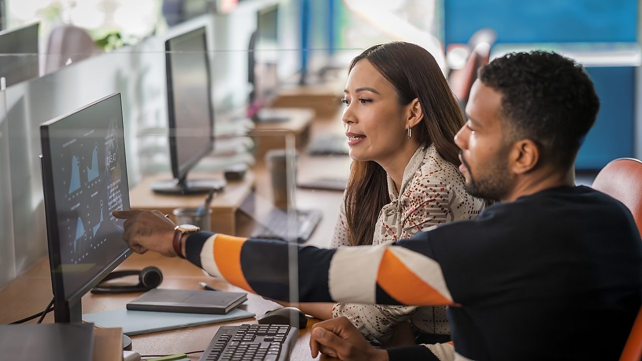 Two colleagues sitting at a desk collaborate while reviewing data visualizations on a computer monitor