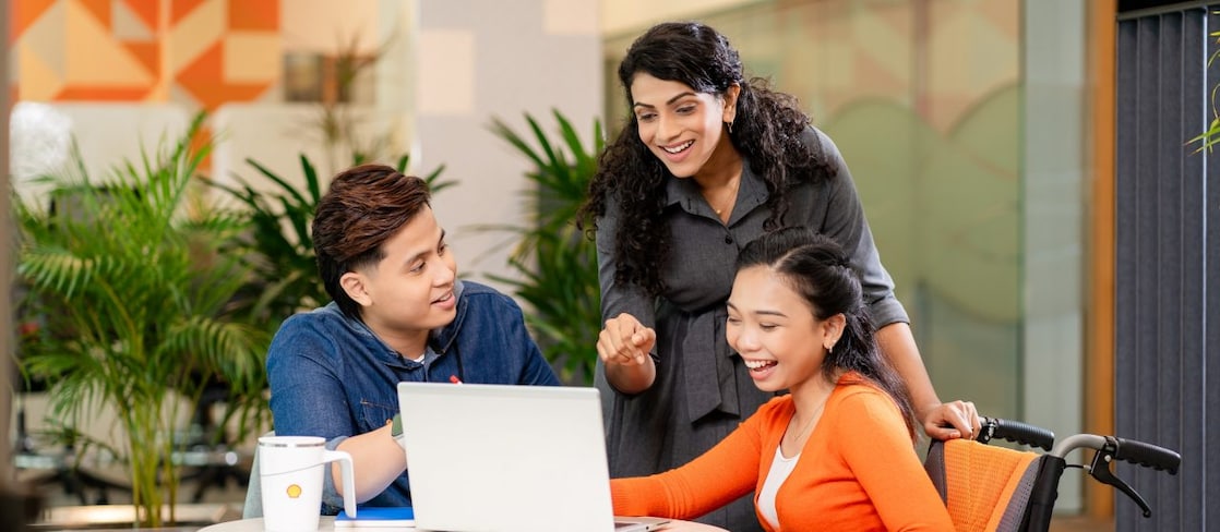 A diverse group of three people at a table, smiling and looking at a laptop