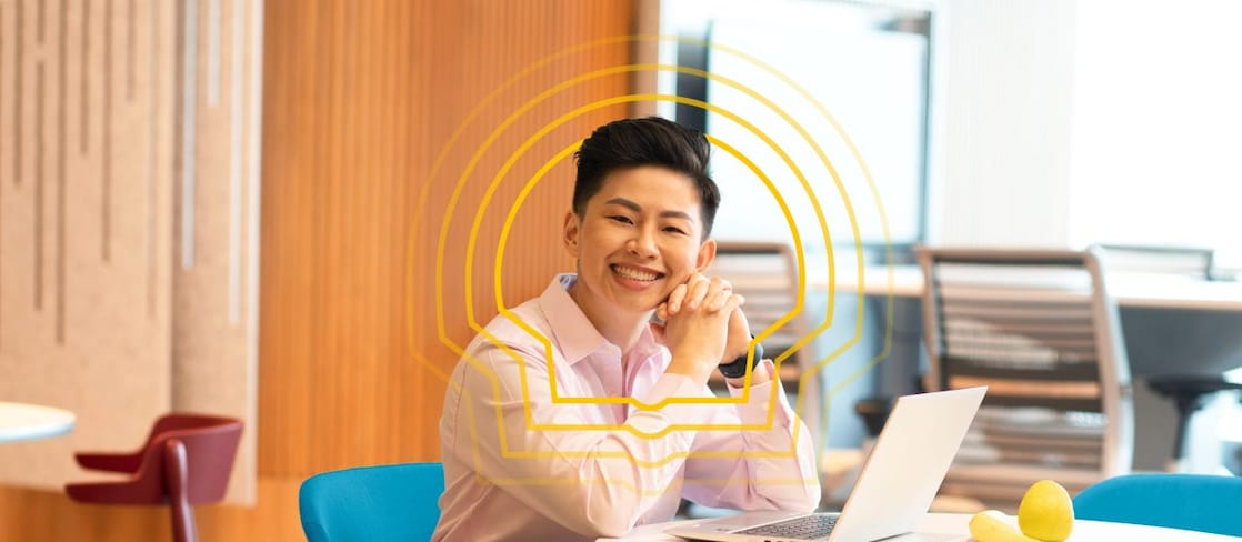 A joyful person in a light pink shirt sits at a round table with a laptop