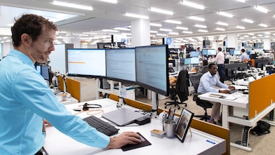 A bustling trading floor shows traders working at multiple computer screens