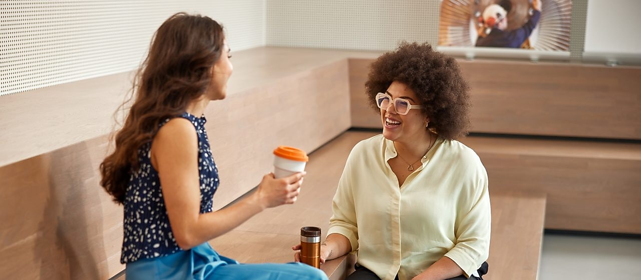 Two women sit on wooden steps, engaged in conversation and smiling