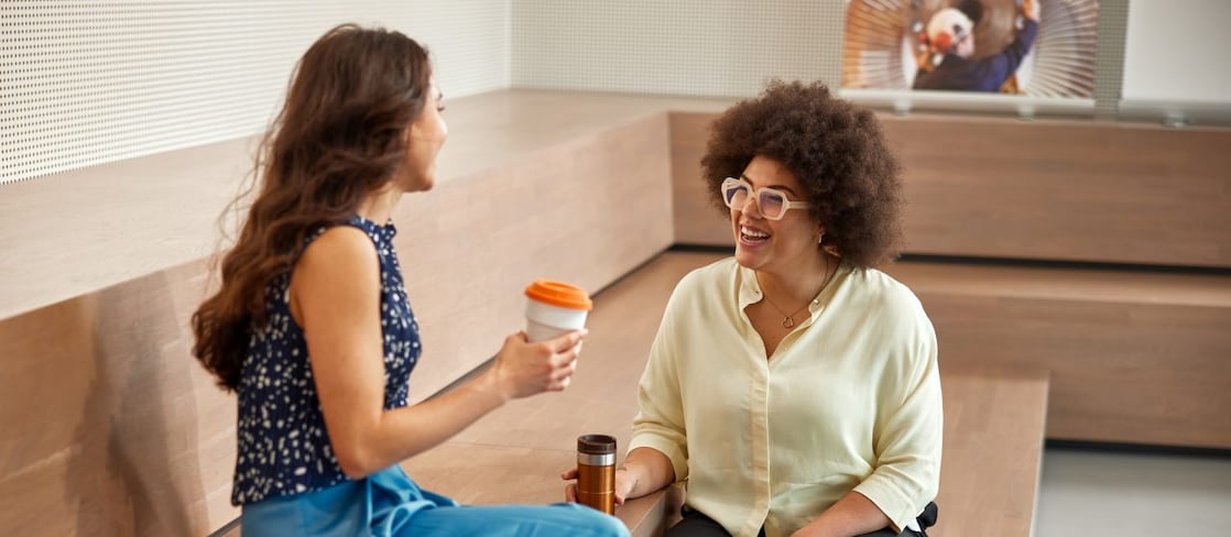 Two women sit on wooden steps, engaged in conversation and smiling