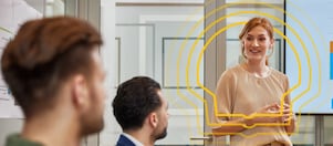A woman smiles while presenting in a modern office, speaking to two attentive colleagues
