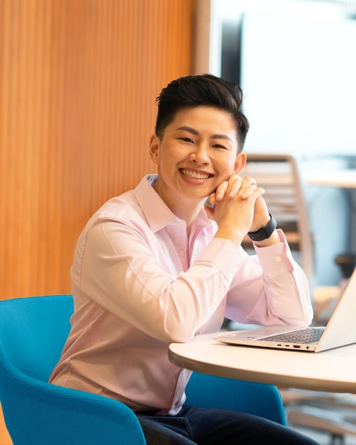 A joyful person in a light pink shirt sits at a round table with a laptop