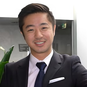 Smiling man in a blazer and tie stands in a modern office with plants in the background
