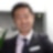 Smiling man in a blazer and tie stands in a modern office with plants in the background