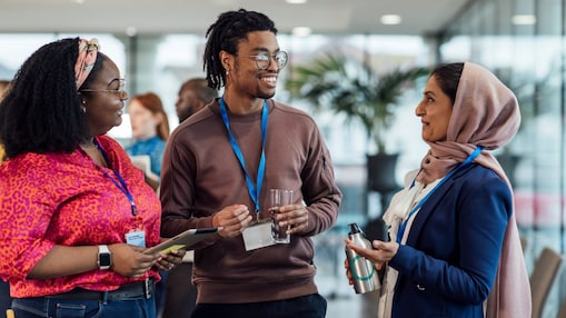 Three people converse at a networking event, smiling warmly