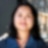 A woman in a blue shirt smiles softly with a blurred urban scene in the background