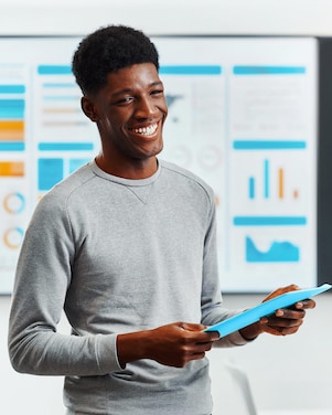 Smiling man holding a blue folder stands in front of graphs and charts