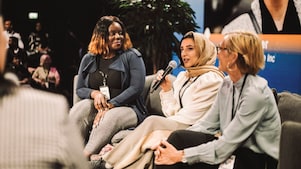 Three women sit together on a panel - one speaks into a microphone, while the others listen attentively