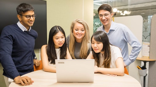 A diverse group of young women and men smiling and looking at the computer screen together.