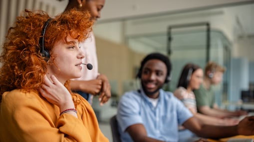 People with headsets on, smiling and sitting in the office.