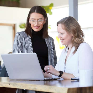 A young woman wearing a blue floral-patterned top smiles at a colleague
