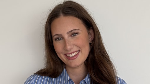 Corporate front portret of a smiling young woman in blue shirt with long dark hair.