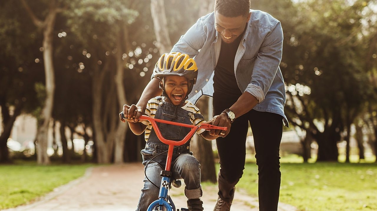 Man teaching a young child how to ride a bike in the park, both smiling