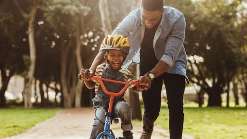 Man teaching a young child how to ride a bike in the park, both smiling