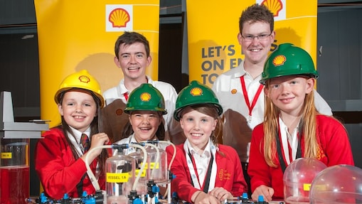 Young school children huddles smiling with Shell employees, in Shell hard-hats