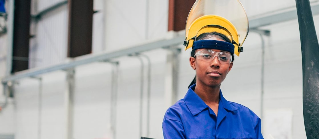 A young woman stands and looks at the camera in an engineering workshop.