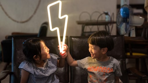 Two small children holding a lightning bolt shaped neon light