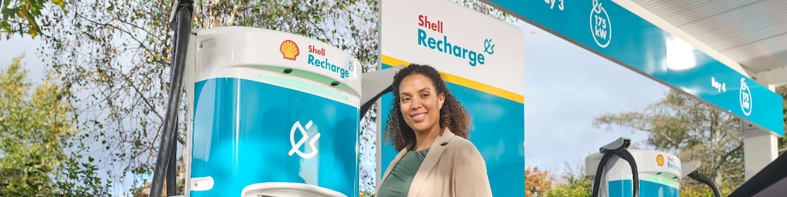 Woman with curly brown hair is pleased to use a Shell Recharge charging station while shopping.