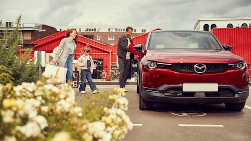 A family of three approach their red electric car after a day out together