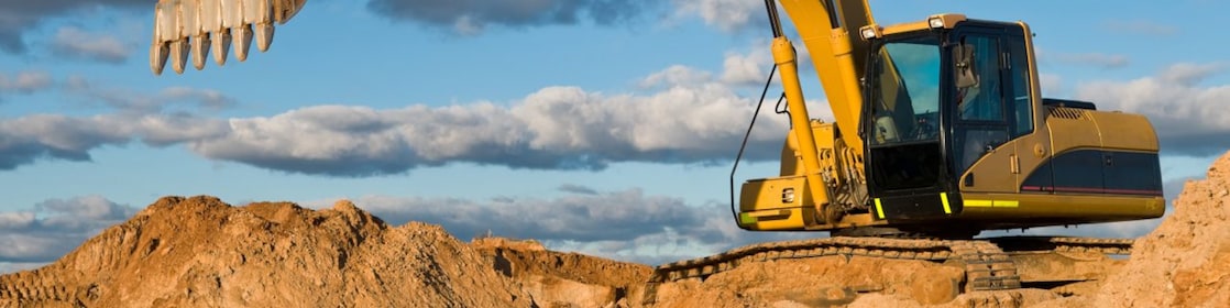 A large yellow excavator is positioned on a mound of dirt, with its arm extended and bucket raised.
