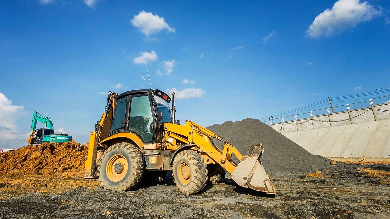A large yellow excavator is positioned on a mound of dirt, with its arm extended and bucket raised.