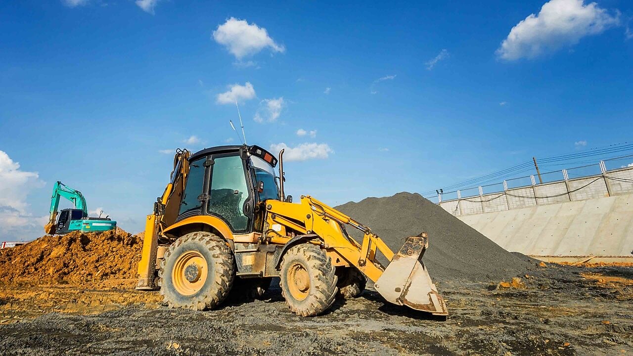A large yellow excavator is positioned on a mound of dirt, with its arm extended and bucket raised.