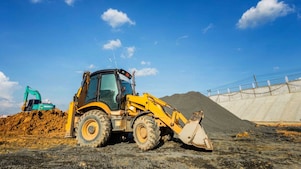 A large yellow excavator is positioned on a mound of dirt, with its arm extended and bucket raised.