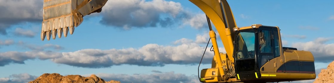 A large yellow excavator is positioned on a mound of dirt, with its arm extended and bucket raised.