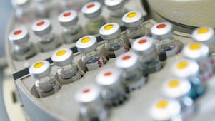 Rows of medicine vials sitting in a holder, some with red dots on the lid, and some with yellow dots on the lid