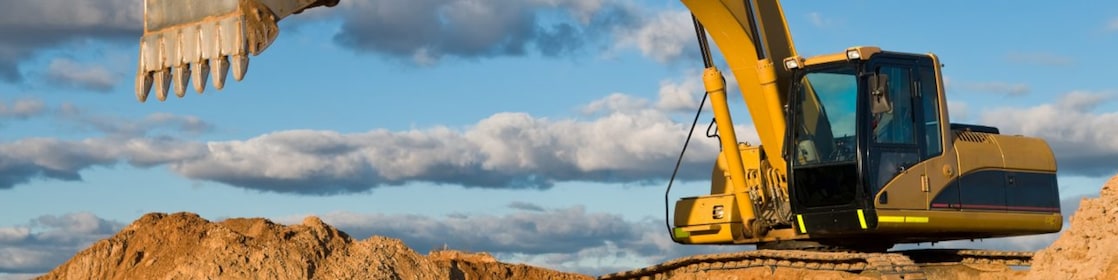 Yellow hydraulic excavator with a large bucket digging into a mound of sand on a construction site, under a blue sky with scattered clouds.
