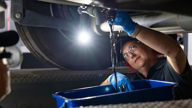 A mechanic drains oil from a vehicle into a blue container in a workshop