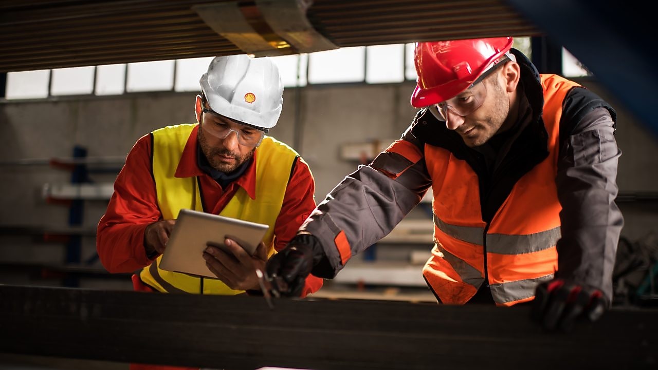 Two workers measuring metal in a factory