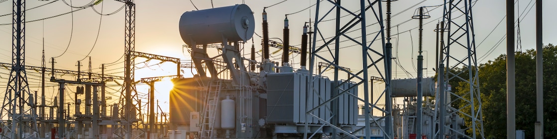 Electrical power substation with interconnected high-voltage transmission lines and equipment at sunset.