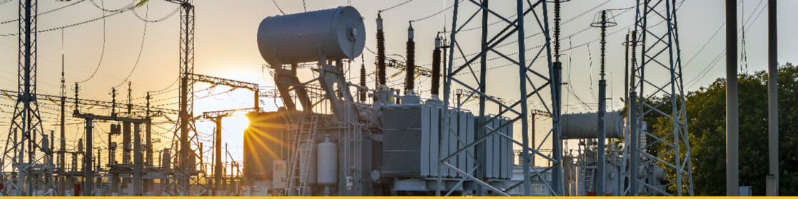 Electrical power substation with interconnected high-voltage transmission lines and equipment at sunset.
