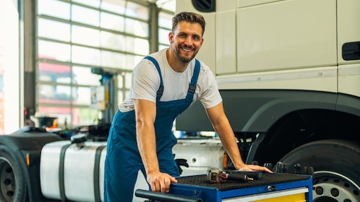 Portrait of positive smiling truck serviceman with tools standing by truck vehicle in workshop. Truck vehicle maintenance and servicing.