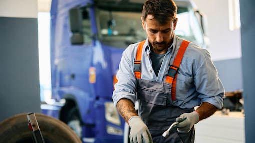 Mechanic using tools to work on a truck in a heavy-duty work shop.