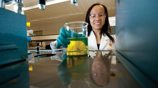 Female scientist reaching out to pick up a glass beaker with some chemical solution inside it