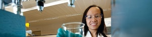 Female scientist reaching out to pick up a glass beaker with some chemical solution inside it