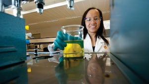 Female scientist reaching out to pick up a glass beaker with some chemical solution inside it