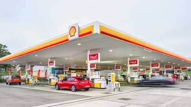 Wide view of Shell petrol station with illuminated canopy, multiple fuel pumps, and cars on the forecourt.
